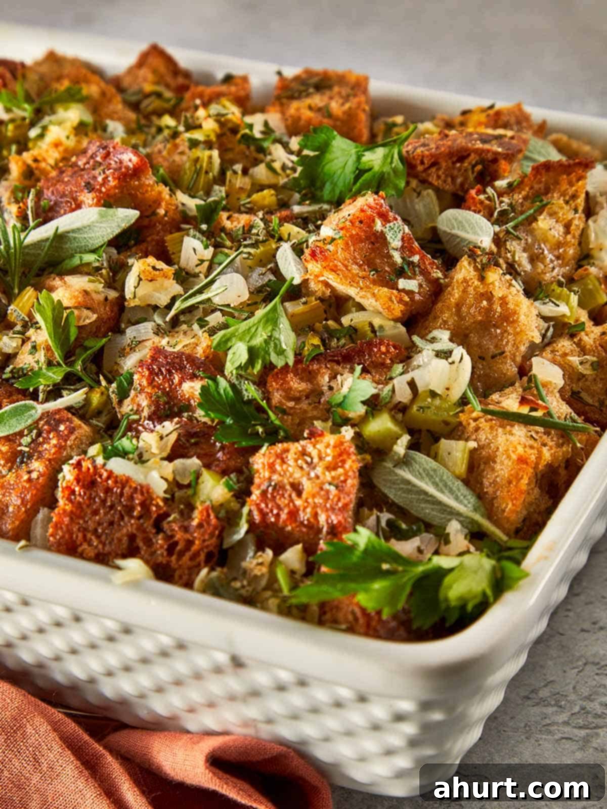 Classic Buttery Herb Stuffing 12 Close-up of a baked herb stuffing with golden bread cubes, sautéed celery and onion, and fresh herbs scattered on top, ready to serve straight from the dish.