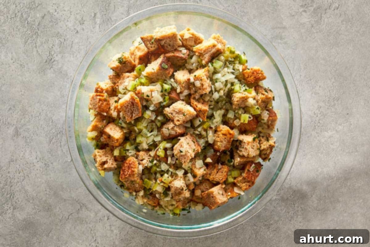 Classic Buttery Herb Stuffing 8 Mixing toasted bread cubes with the cooked onion, celery, and herb mixture in a large glass bowl for homemade stuffing.
