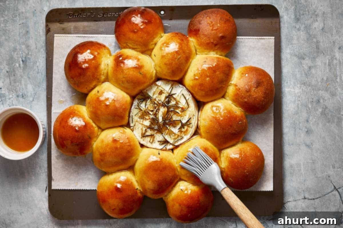 A baked wheel of Camembert surrounded by golden sweet potato buns, with a drizzling of honey and a sprinkle of flaky salt and fresh rosemary for a perfect finish