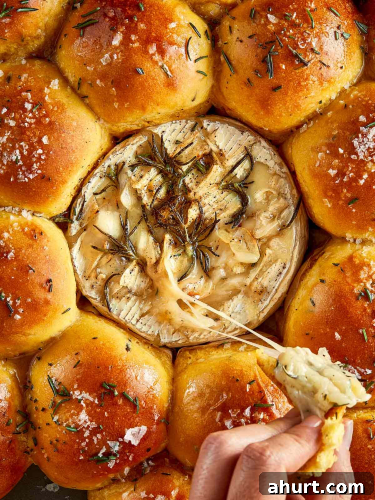Close-up shot of a perfect golden sweet potato bun being pulled from the tray, with the melted Camembert cheese gleaming in the background