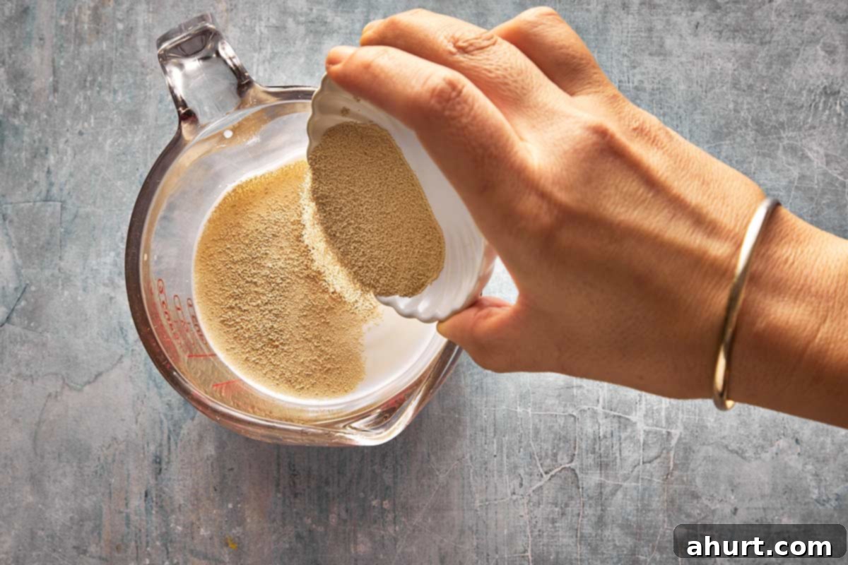 Top-down shot of a pitcher with water, milk, sugar, and dry yeast being poured in, illustrating the yeast activation step