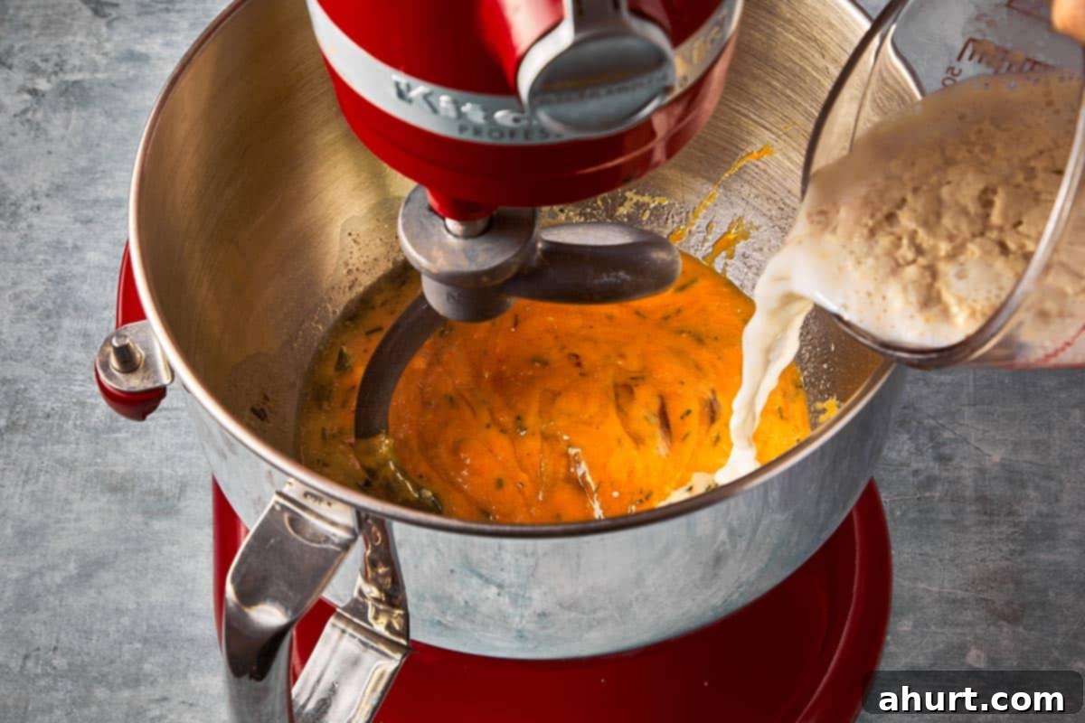 A stand mixer bowl with the initial dough mixture being poured in, showing the wet ingredients combined