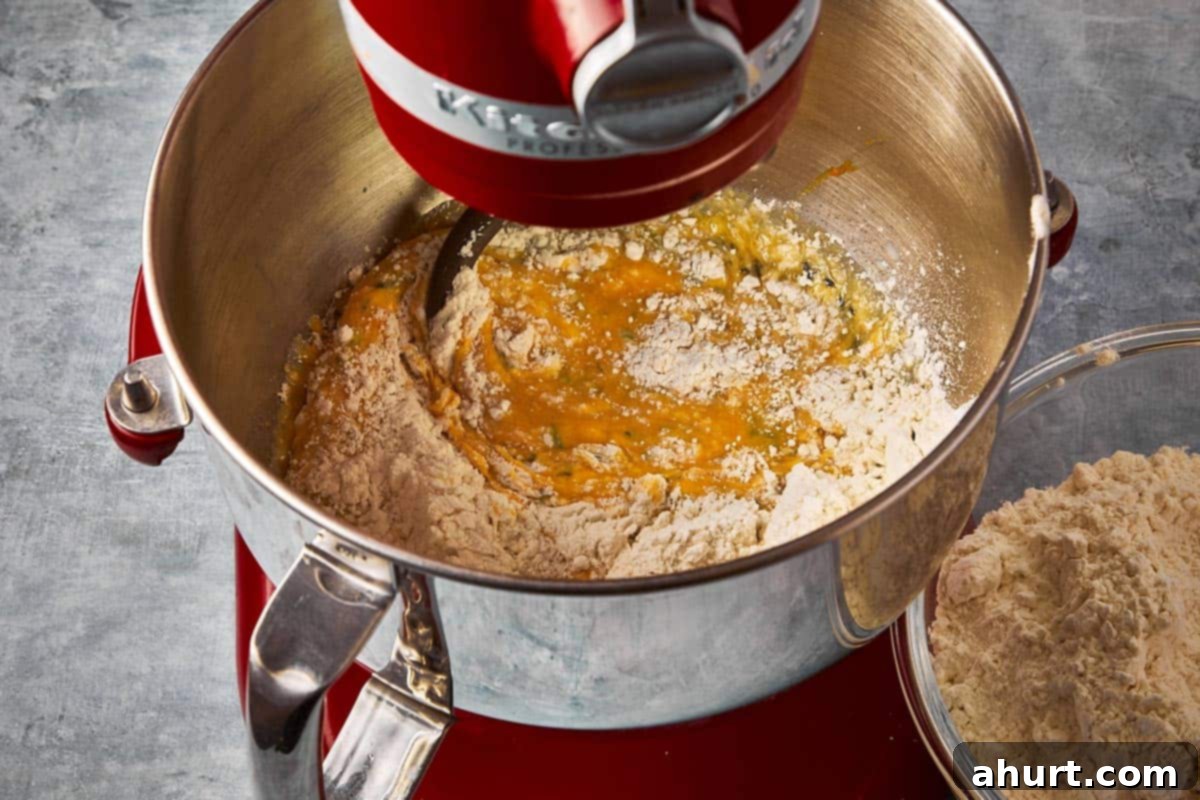 A stand mixer with the base of a bread dough, with all-purpose flour gradually being added in, demonstrating the dough formation process