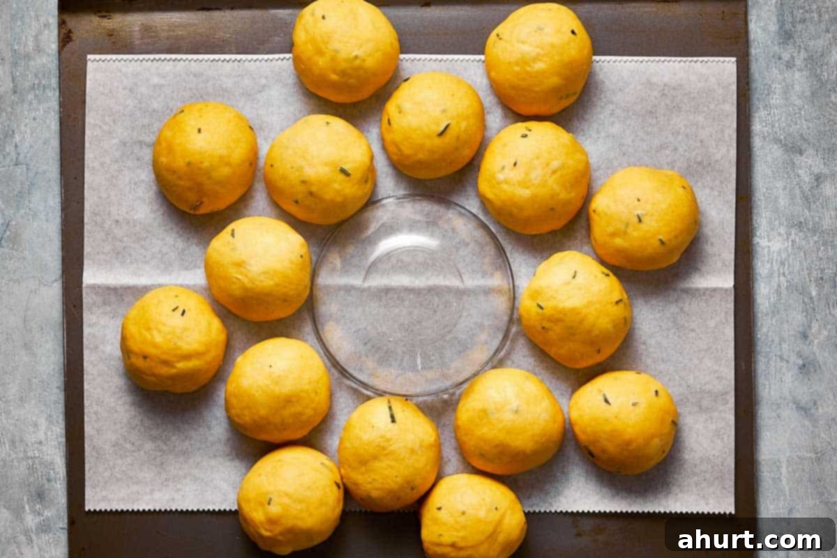 Small, round balls of sweet potato dough arranged around an oiled glass bowl on a baking tray, showing the second proofing stage