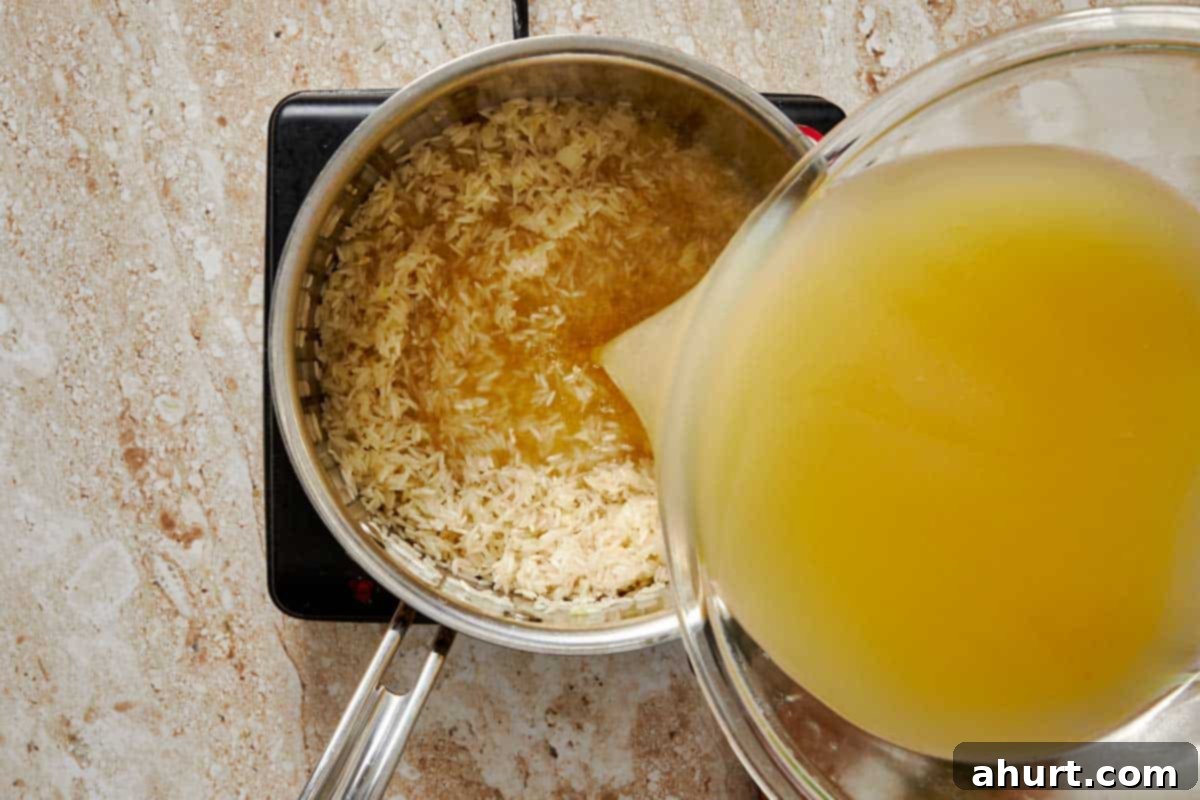 Simple and Flavorful Garlic Butter Rice 6 Chicken bone broth being poured into the pot with sautéed garlic butter rice, along with dried parsley, salt, and pepper.