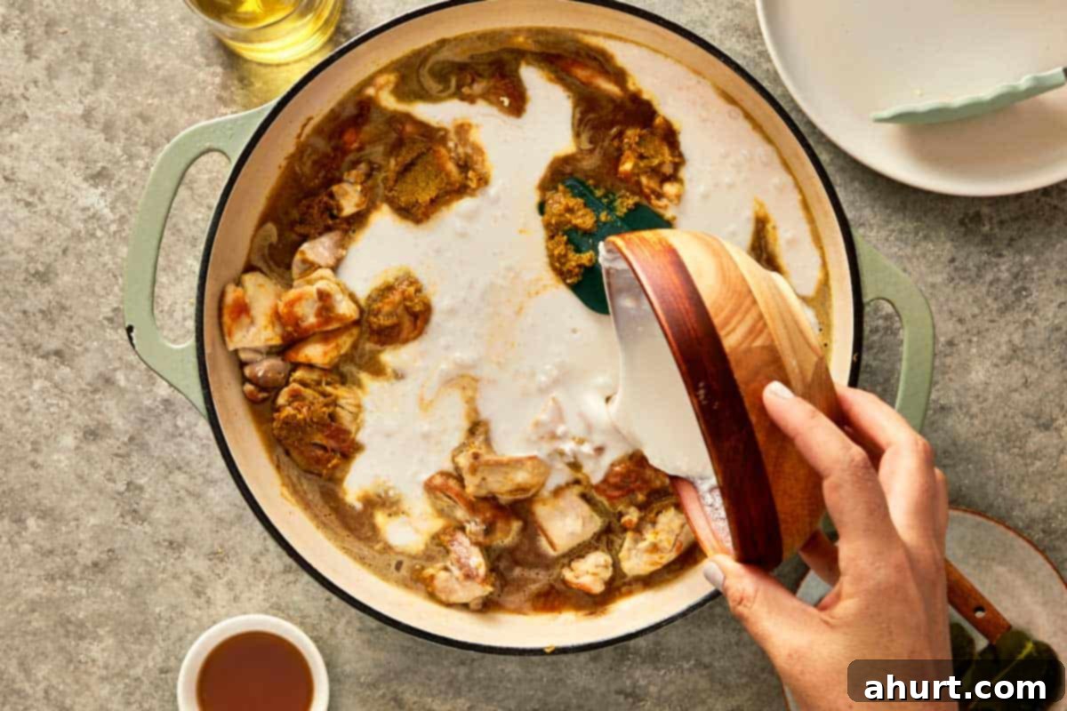 top down shot of a pan with chicken thigh, chicken stock, coconut milk, palm sugar, fish sauce, and kaffir leaves. 