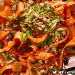 Ginger Peanut Carrot Slaw 11 Delicious Asian Carrot Salad with crushed peanuts on top, served in a white bowl with a spoon on the side