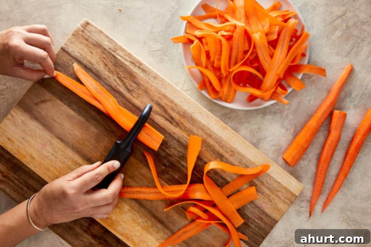 Ginger Peanut Carrot Slaw 4 Fresh carrots being peeled into thin ribbons using a vegetable peeler over a cutting board