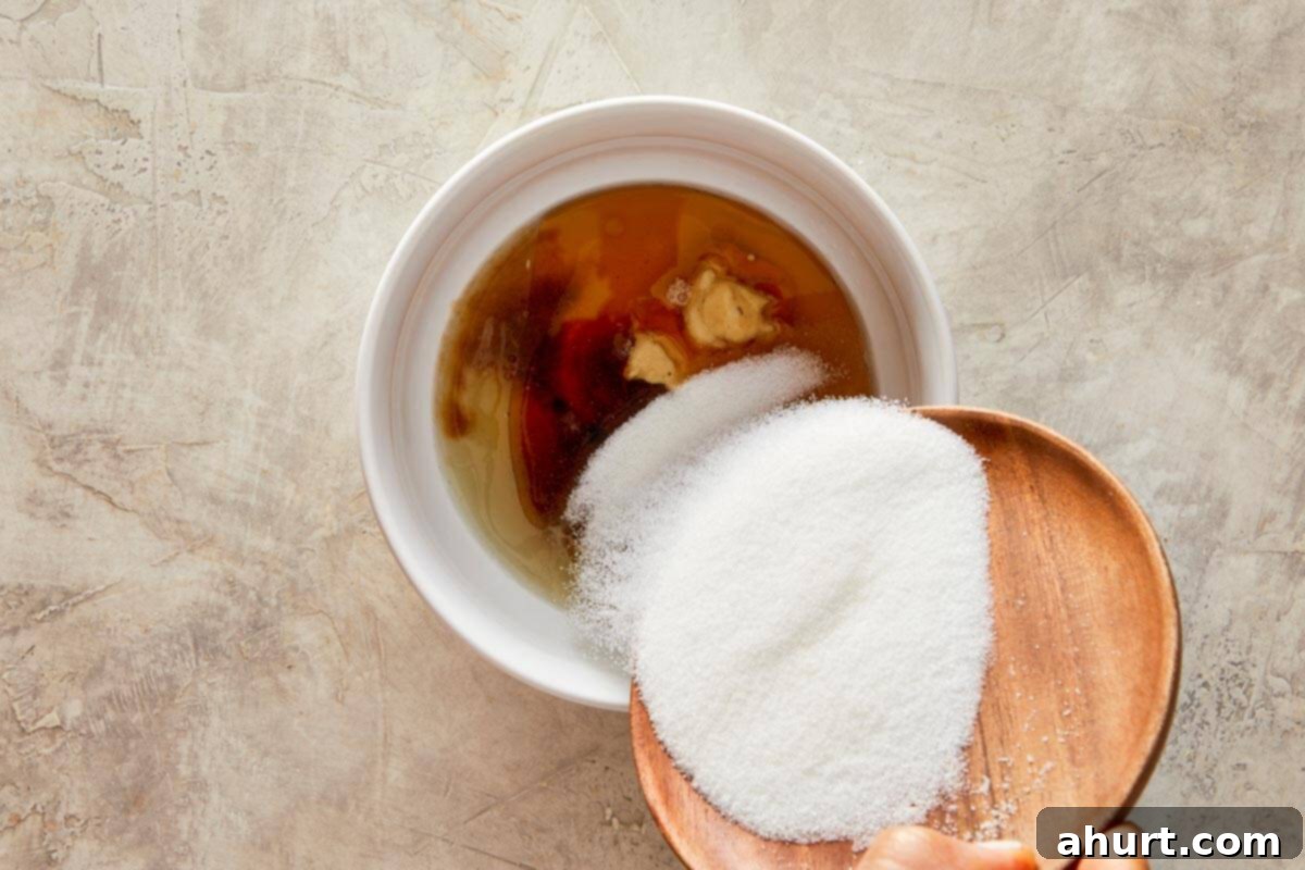 Ginger Peanut Carrot Slaw 5 A bowl containing the whisked dressing ingredients: sugar, lemon and lime juice, mirin seasoning, mustard, sesame oil, and soy sauce