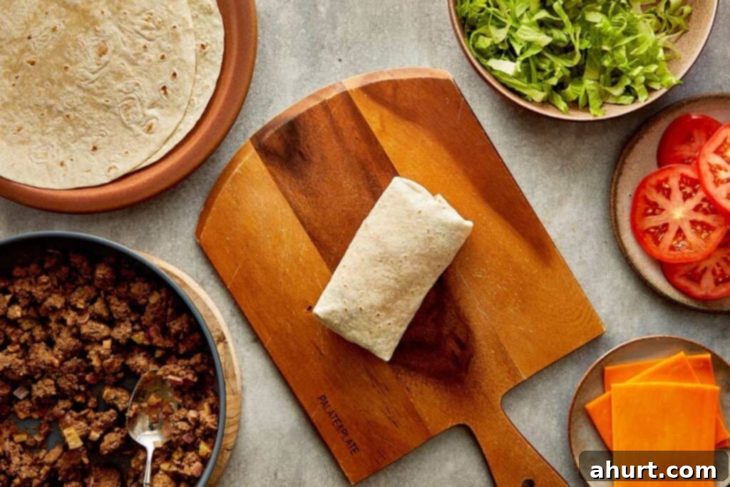 Cheeseburger Bliss Wrap 17 Two hands making a tortilla wrap with mince and lettuce on a benchtop.