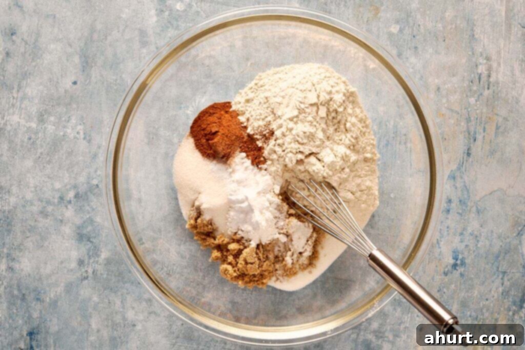A top-down shot of a clear glass bowl filled with dry ingredients, such as flour and cocoa powder, alongside a metal whisk resting on the bowl's edge.