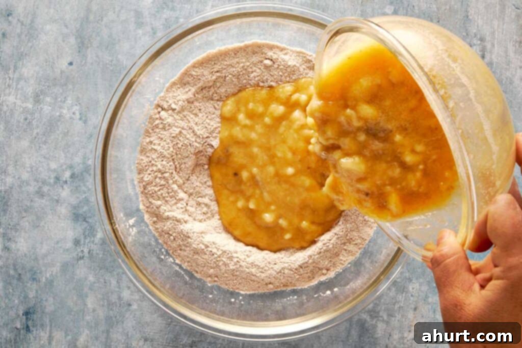A top-down shot of a bowl of flour as wet ingredients are being poured into it from directly above the bowl.