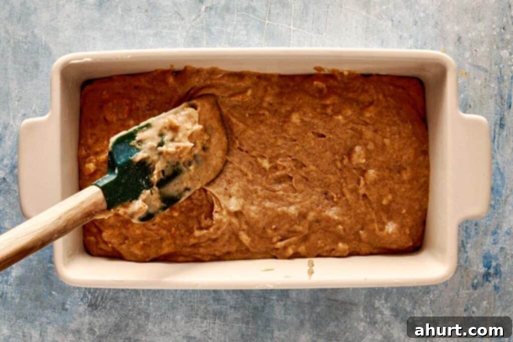 A top-down shot of green spatulas being used to fill a rectangular loaf pan lined with parchment paper.