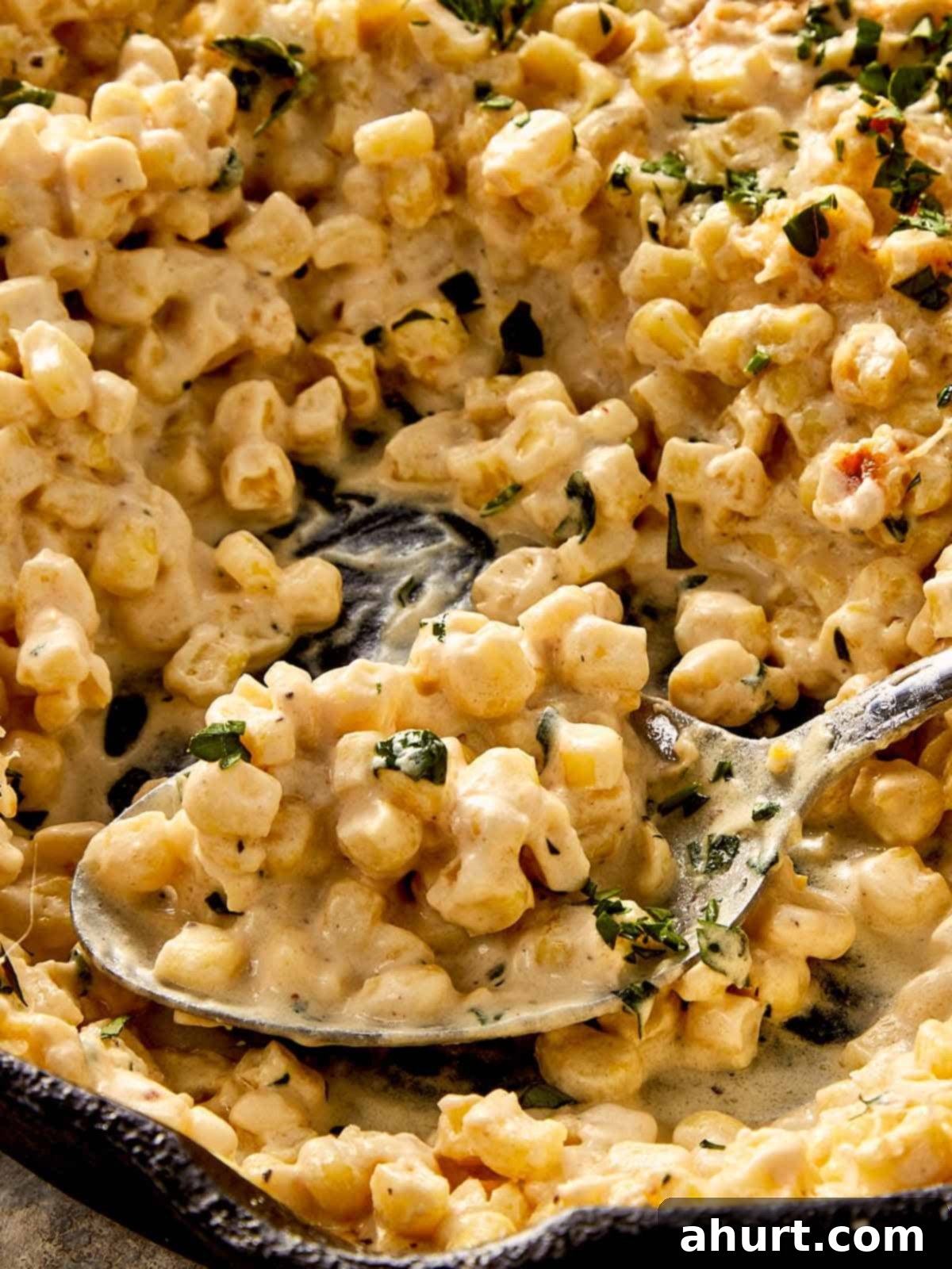 Creamy corn with melted parmesan and fresh parsley, scooped from a pan with a spoon