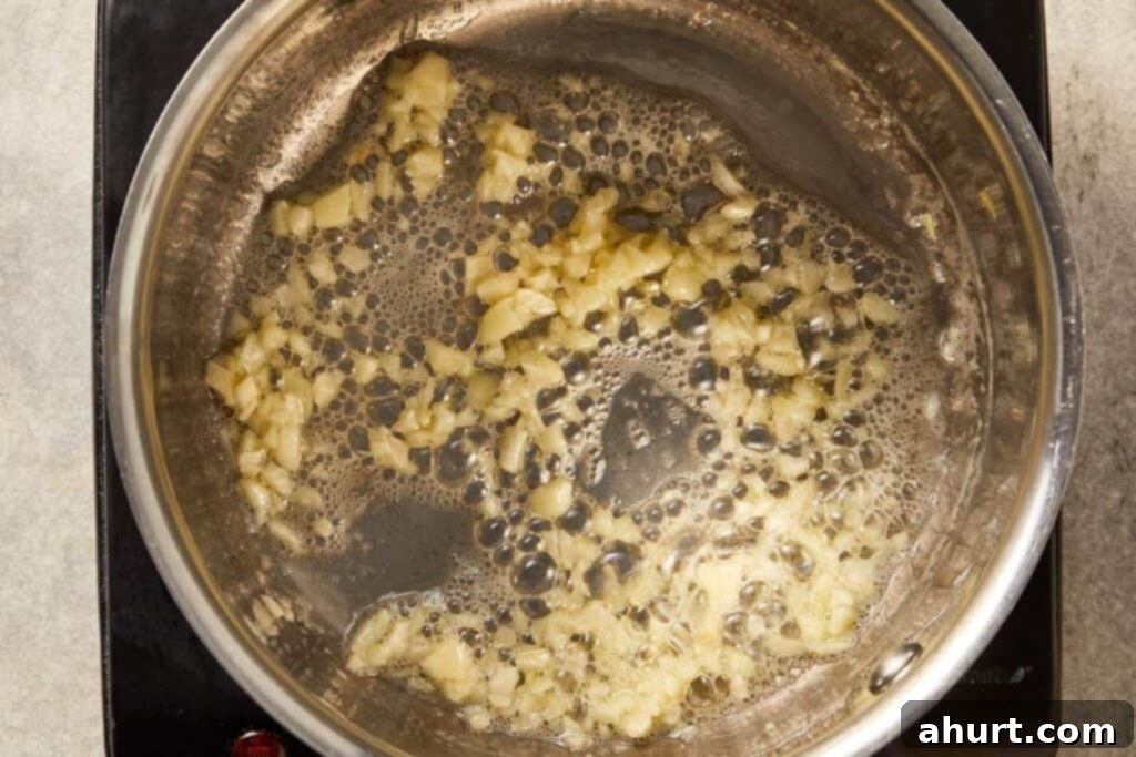 Minced garlic cooking in melted butter in a pan, becoming fragrant for creamy corn recipe