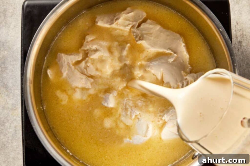 Light cream being poured into a pan with cream cheese and chicken stock to create a smooth base for creamy corn