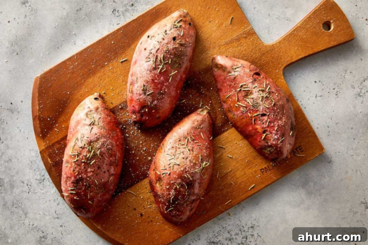 Raw sweet potatoes seasoned with salt, pepper, and herbs on a wooden cutting board, ready to be baked