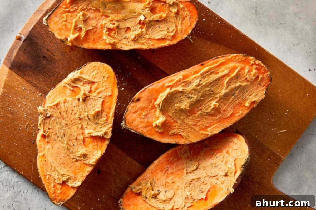 Baked sweet potatoes cut open and spread with garlic butter on a wooden board