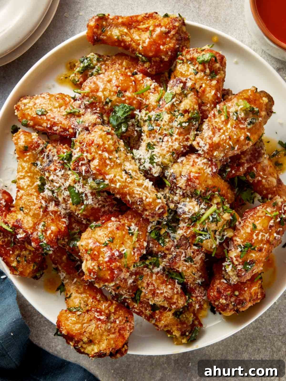 crispy garlic parmesan chicken wings coated in garlic butter, parmesan and herbs, served on white plate