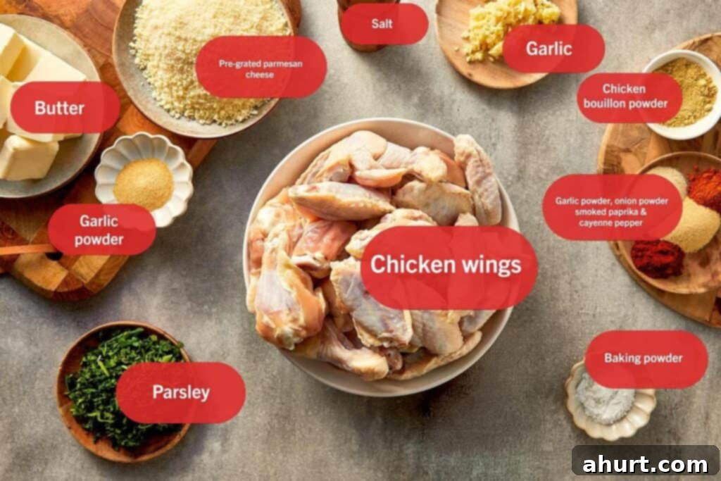 Garlic parmesan chicken wings ingredients laid out on a table, including raw chicken wings, butter, pre-grated parmesan cheese, garlic cloves, garlic powder, onion powder, smoked paprika, cayenne pepper, chicken bouillon powder, salt, parsley, and baking powder